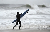 10月28日，一名冲浪爱好者在美国纽约长滩海边紧紧抱着冲浪板抵抗着大风。当日，飓风“桑迪”从加勒比海...